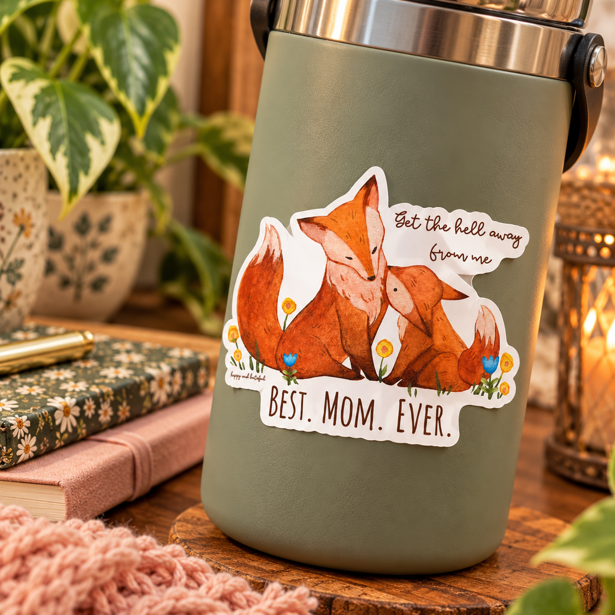 An insulated tumbler with a matte sage green body and stainless steel rim, featuring a die-cut sticker of a mother fox and her cub with the text 'get the hell away from me' and 'BEST. MOM.EVER'