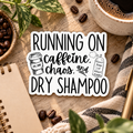 A die-cut sticker with the phrase “RUNNING ON caffeine, chaos, and DRY SHAMPOO” in black lettering on a white background, surrounded by coffee beans, a notebook, a cup of coffee, and green leaves on a wooden surface.