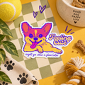 A colorful die-cut sticker featuring a cartoon dog with the text 'Feeling Cute might go chew a shoe later', styled on a yellow and green checkered mat with dog toys and treats around it.