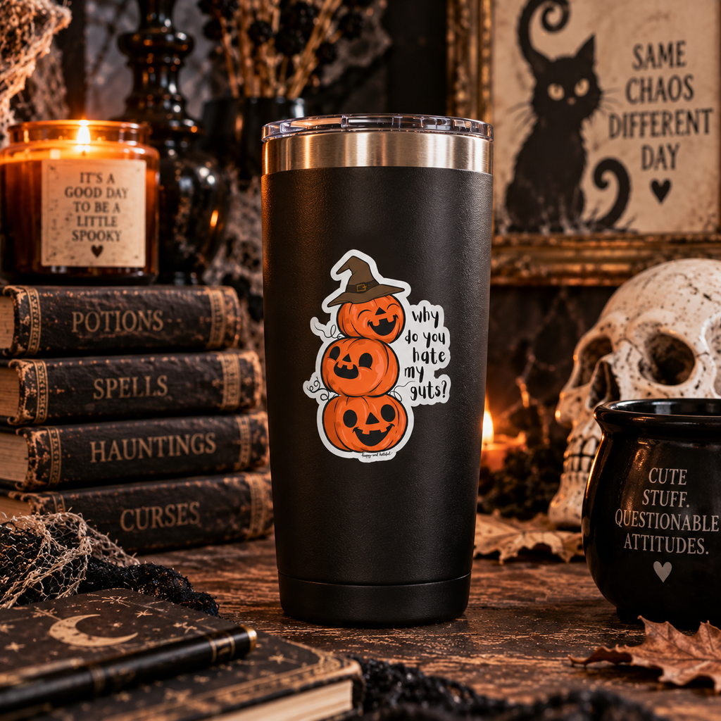 A black insulated tumbler with a stainless steel lid stands on a rustic tabletop surrounded by Halloween decor, including stacked books, a candle, a skull, and a black mug. The tumbler has a sticker featuring  three stacked jack-o'-lanterns wearing a witch hat with the text 'why do you hate my guts?' 