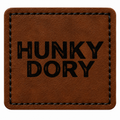 A square brown patch with rounded corners, featuring the words 'HUNKY DORY' printed in bold black capital letters in the center. The patch has a stitched border and is shown against a plain white background.