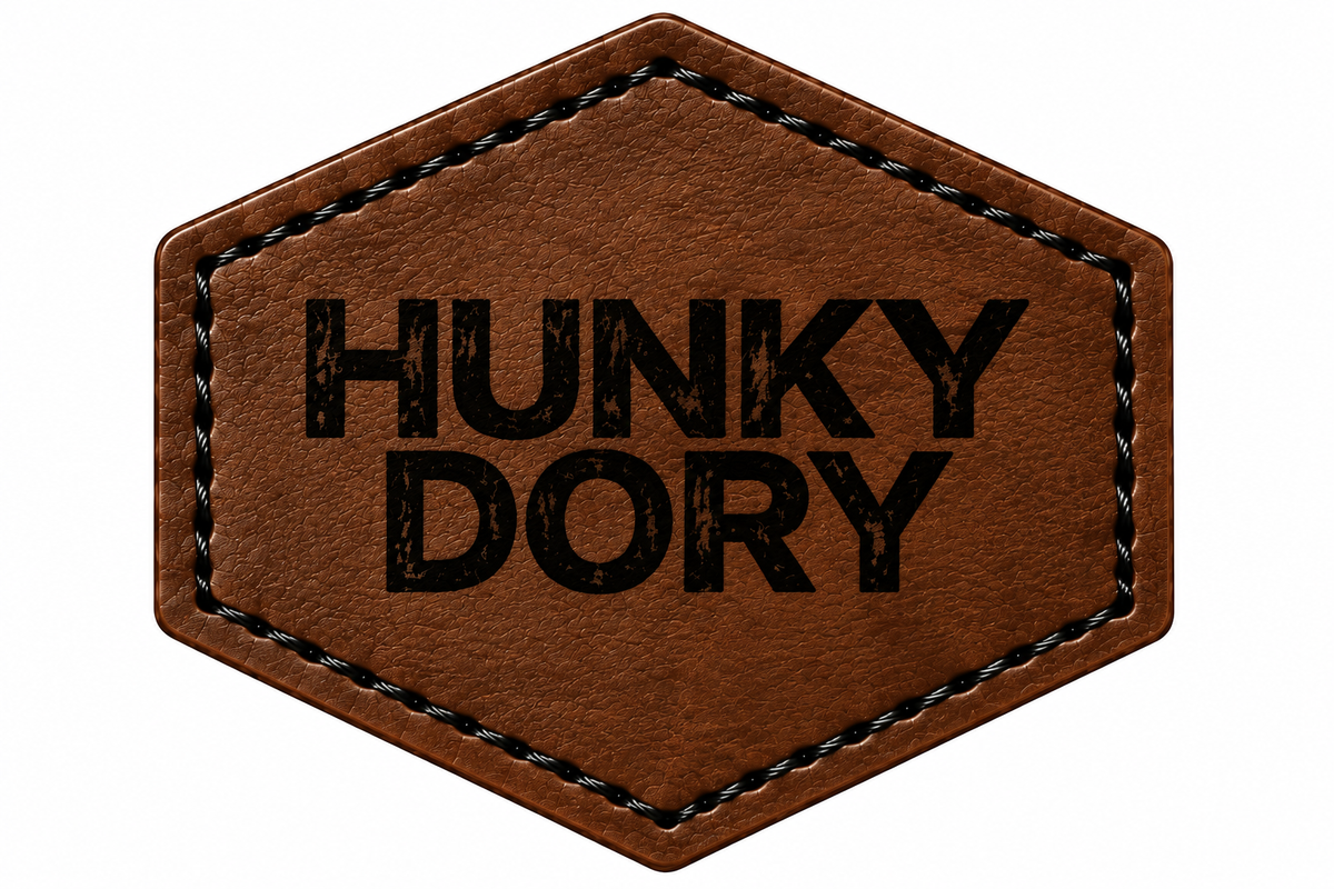 A hexagonal brown patch with black stitched border and the text 'HUNKY DORY' engraved in black on a white background.