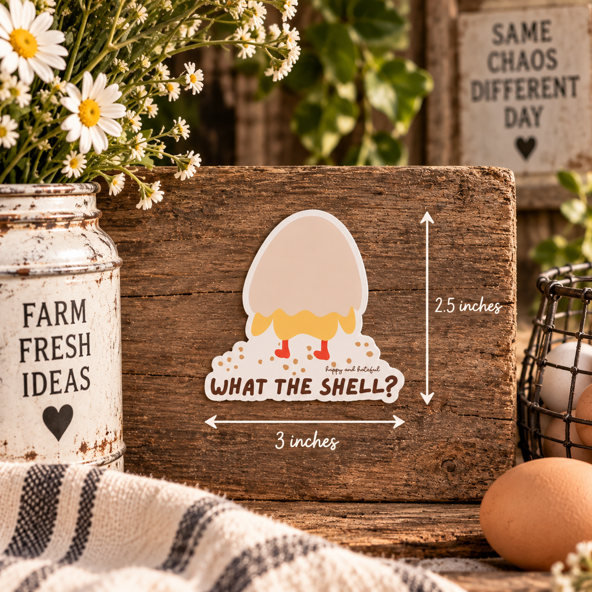 A rustic wooden board featuring a sticker of a cartoon eggshell cracking open to reveal the bottom half of a chicken, with the text 'WHAT THE SHELL?'. White dimension arrows on the image indicate size.