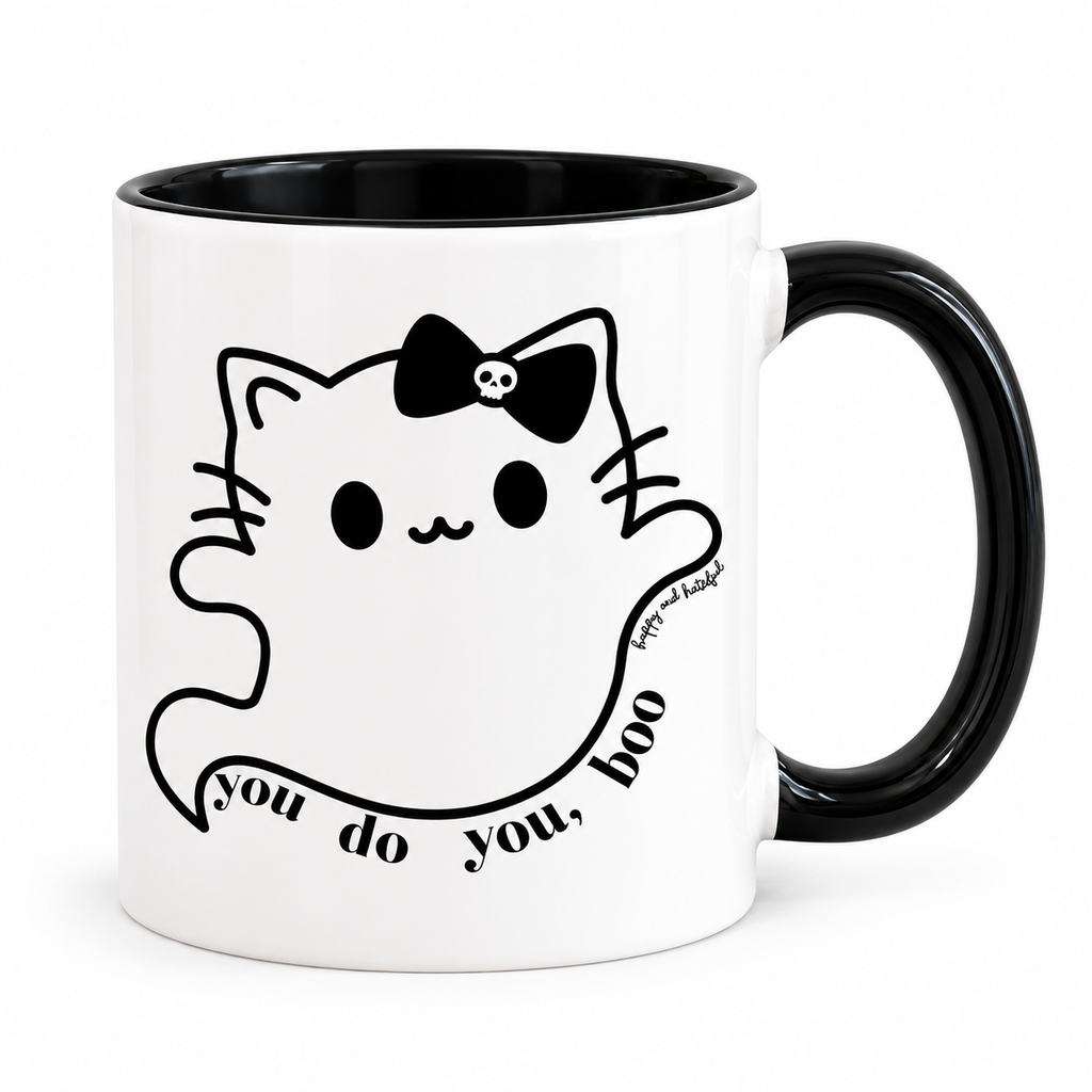 A white ceramic mug with a black interior and black handle, featuring a black line art graphic of a cat wearing a skull-adorned bow and a banner that reads 'you do you, boo'.